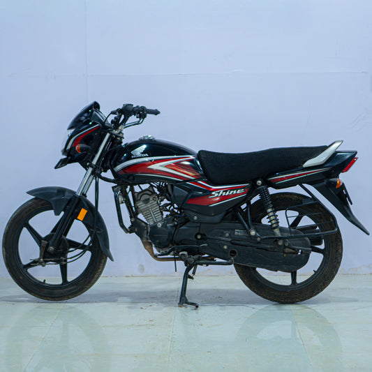 Honda Shine 100 motorcycle from BikeDilwado, showing the front view with headlight, handlebars, and sleek body design.