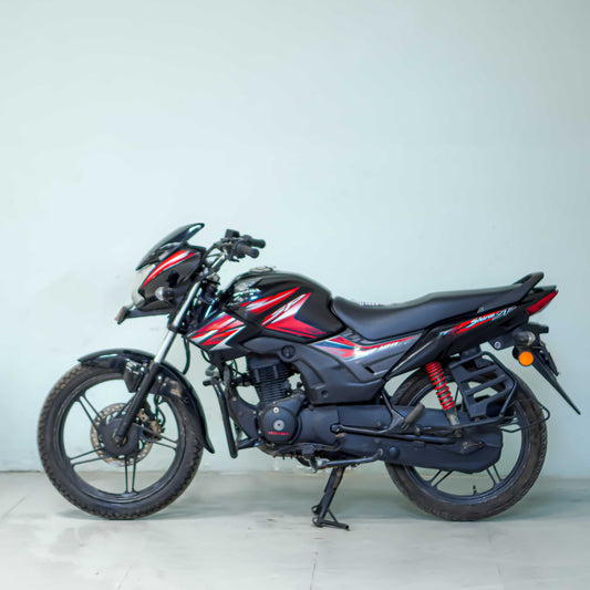Honda CB Shine 125 motorcycle with chrome exhaust and black alloy wheels, parked on a street.