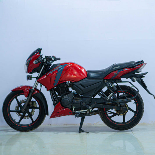 Red TVS Apache 160 motorcycle parked on the road, showcasing its sporty design and sleek black and red color scheme.