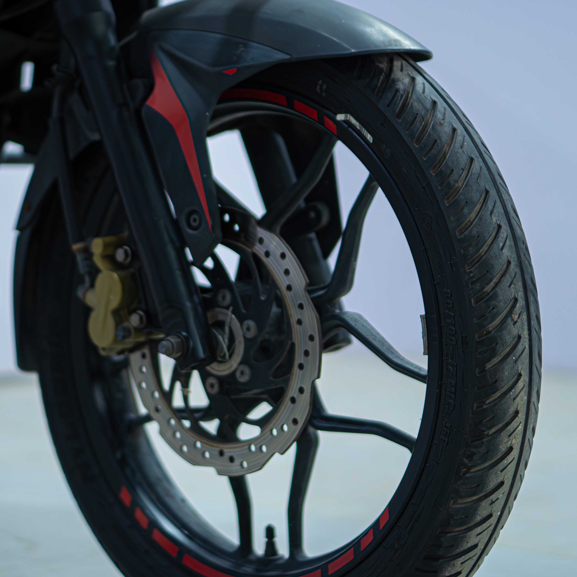 Red Bajaj NS 160 motorcycle parked on a street, showcasing its sporty design and sleek body in natural outdoor lighting.