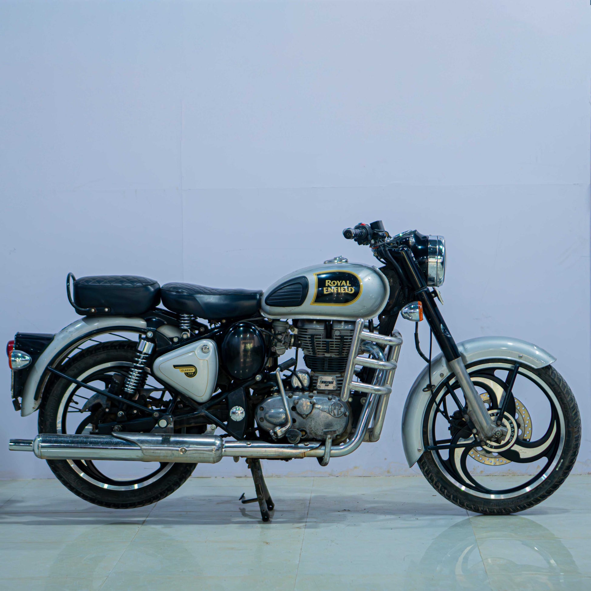 Royal Enfield Classic 350 motorcycle displayed outdoors with a vintage design and chrome accents, shown from the side.