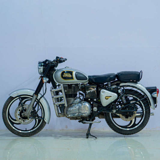 Royal Enfield Classic 350 motorcycle with black fuel tank, chrome accents, and vintage styling, parked on a scenic road.