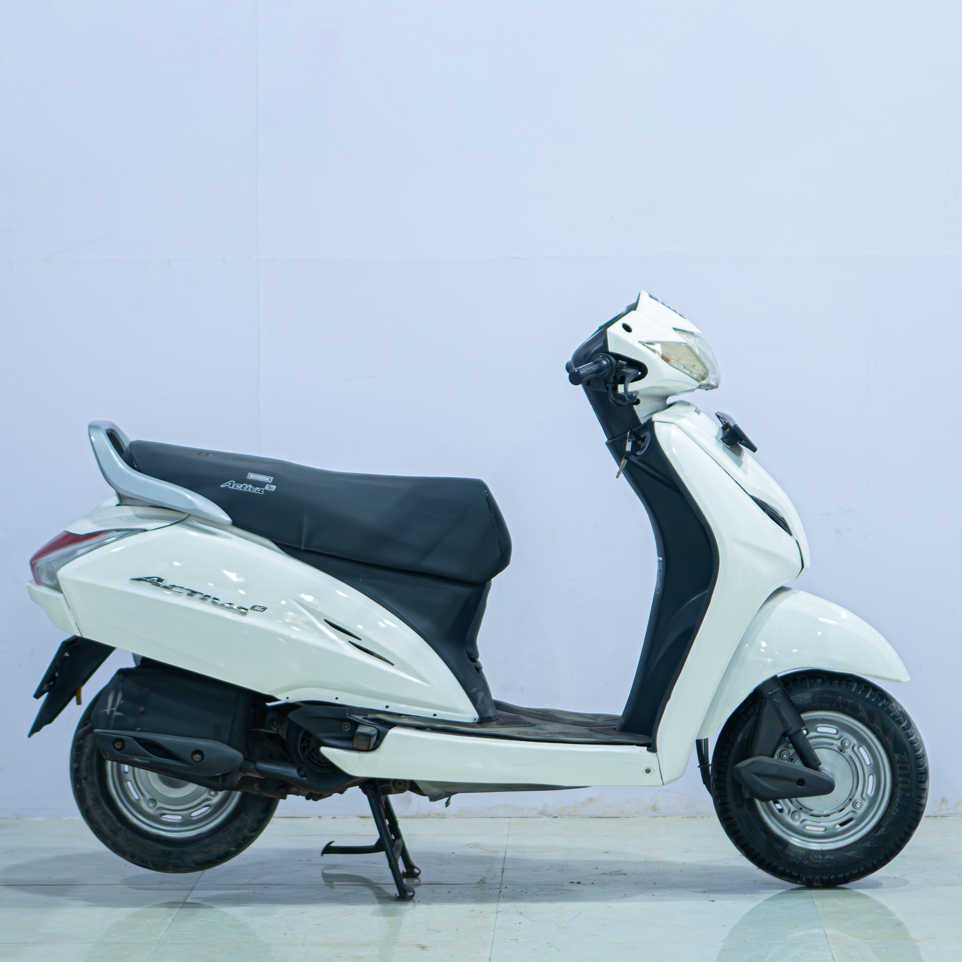 Honda Activa 3G scooter with black body and silver accents, parked on a city street, showcasing its modern design.