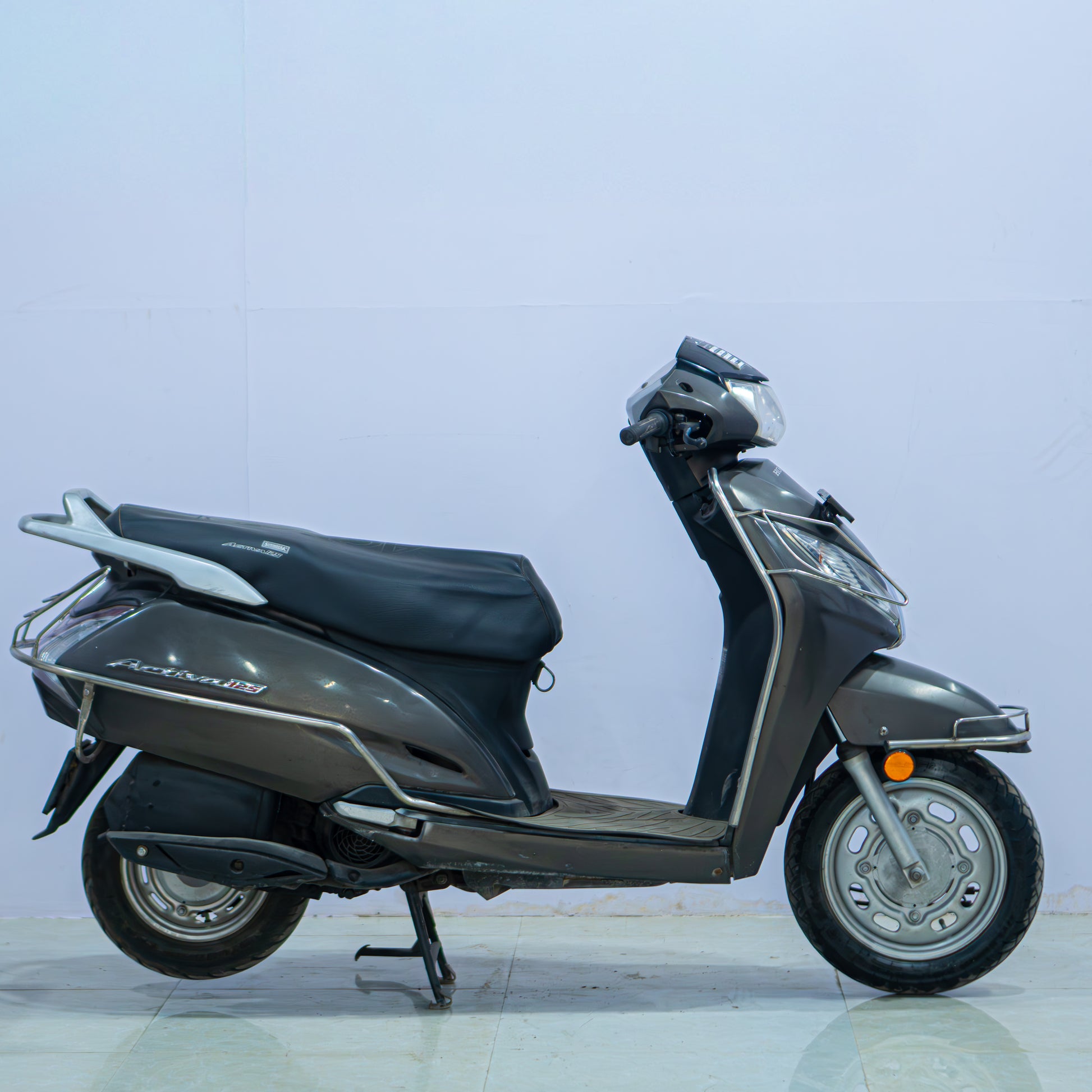 Honda Activa 125 scooter with black seat and silver body, parked on a street with a clear background.