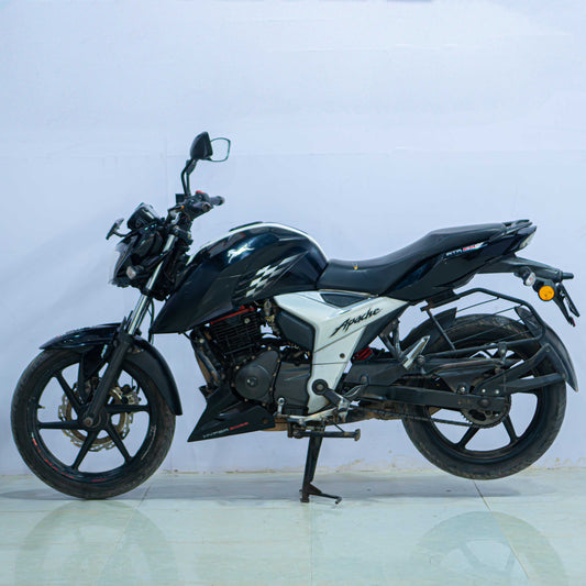 Red TVS Apache 160 4V motorcycle with sporty design and sleek body, parked on a city street.