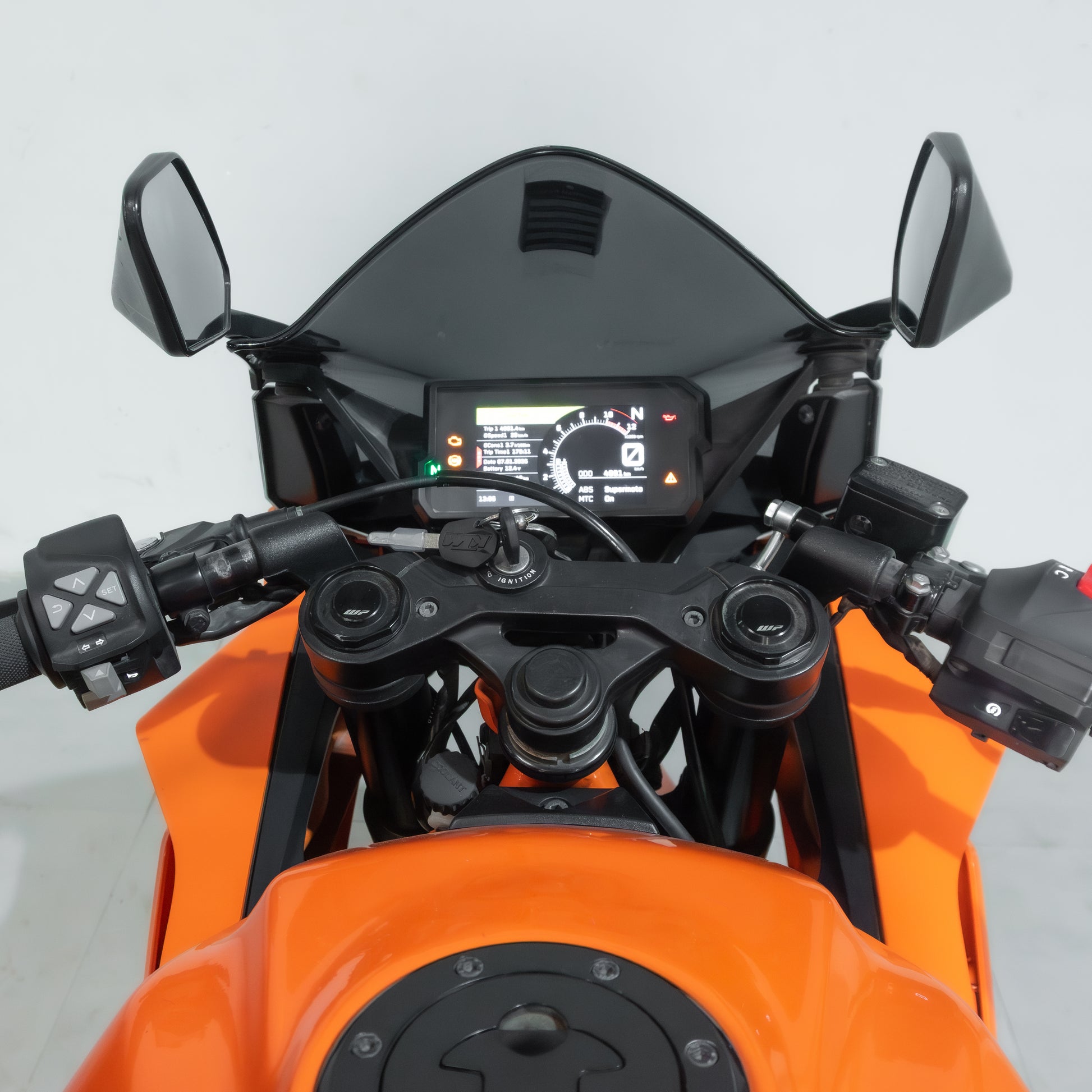 Close-up of an orange motorcycle's handlebar and dashboard on a white background