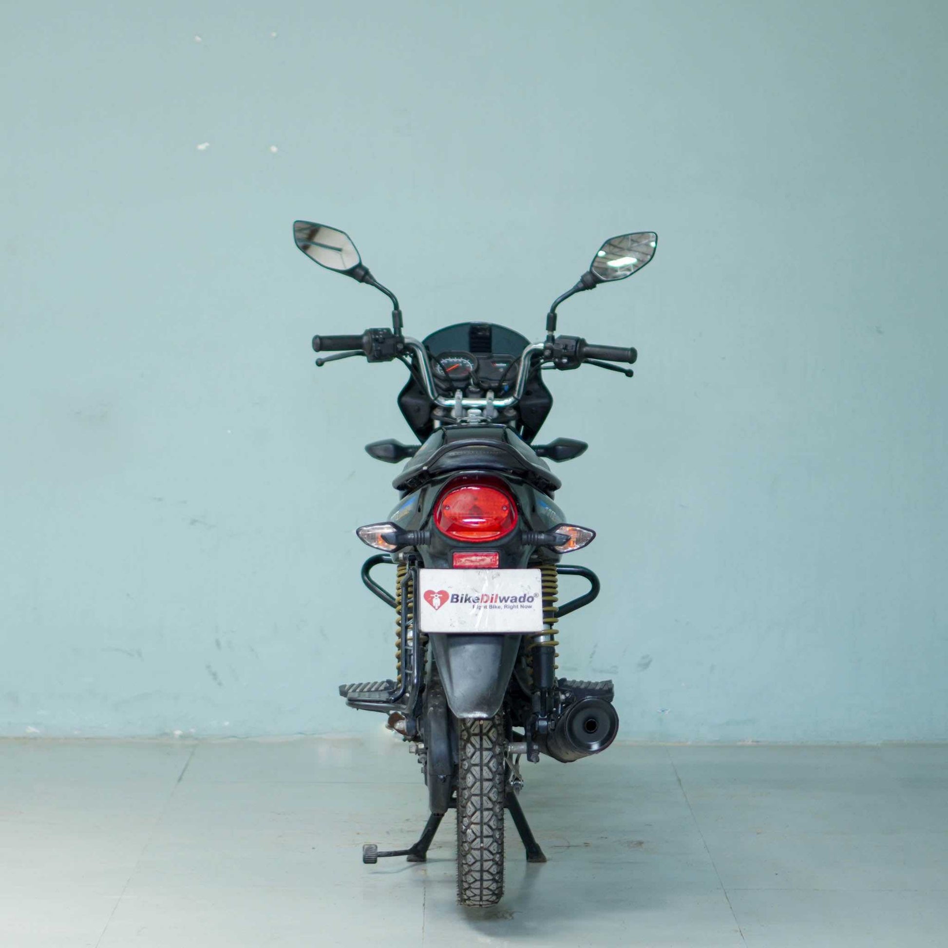 Bajaj Platina motorcycle with black and silver body and chrome exhaust, parked on a road.