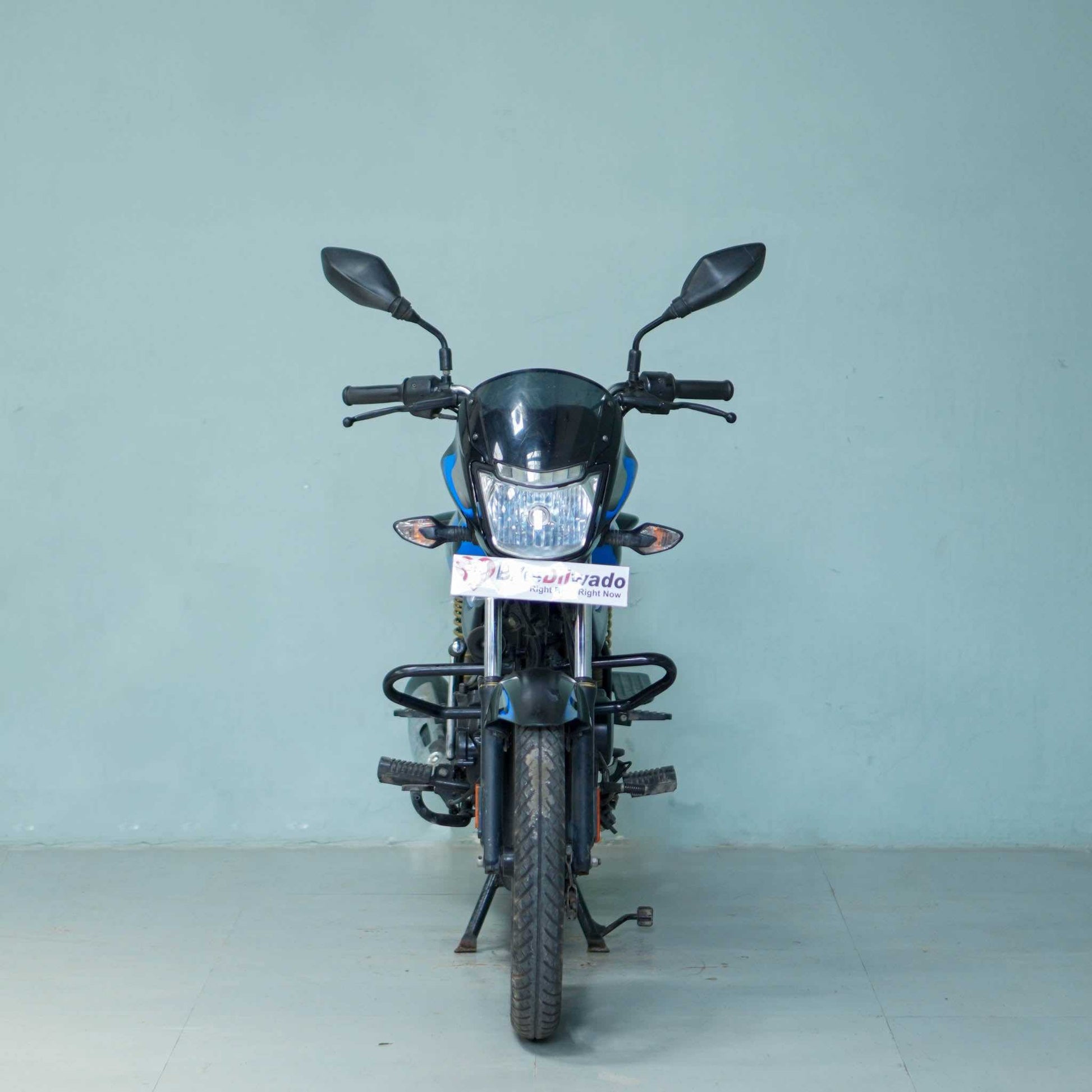 Bajaj Platina motorcycle parked on a street, showcasing the sleek silver and black design with the BikeDilwado branding.
