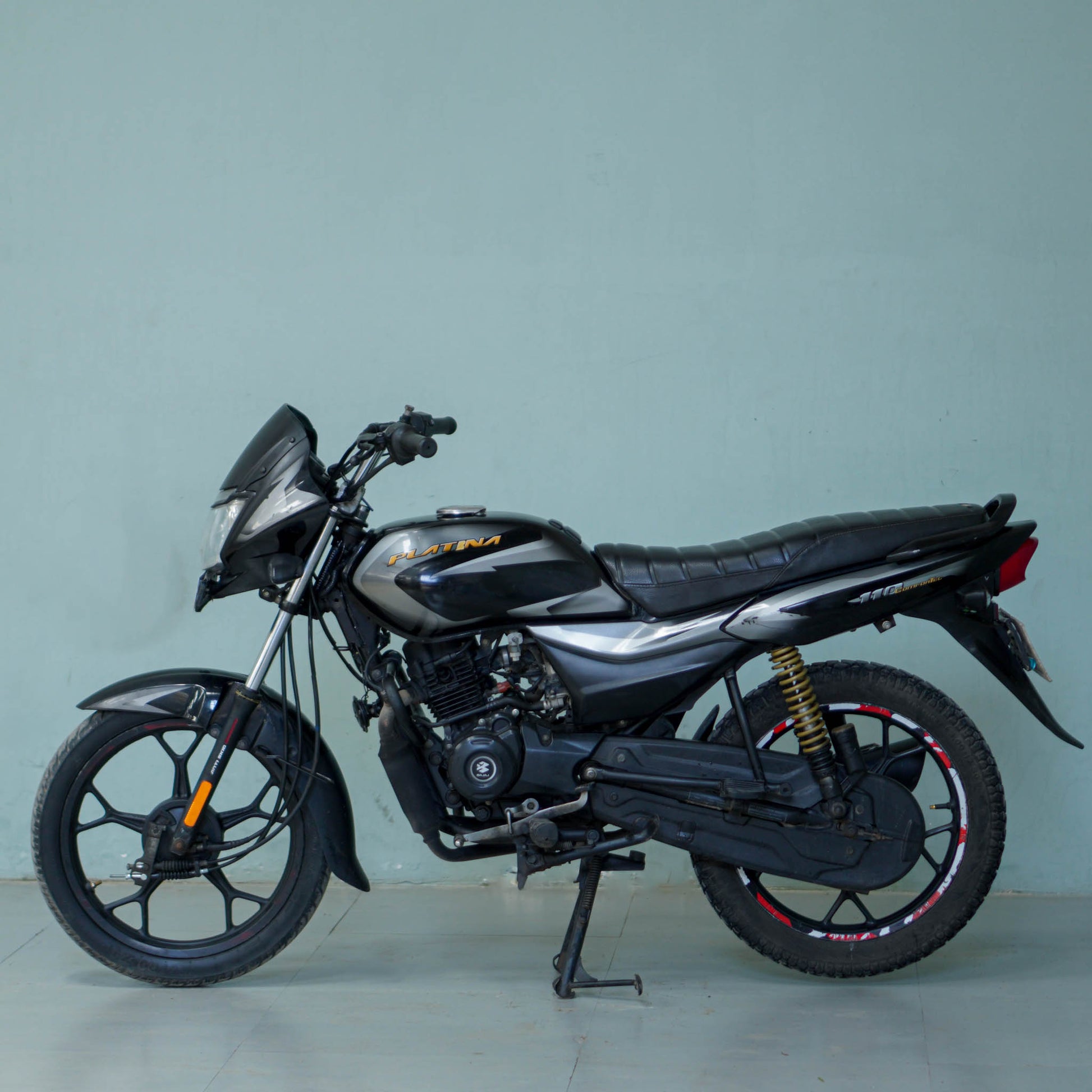 Bajaj Platina motorcycle with black and silver body, front view showing headlight and handlebar, parked outdoors.