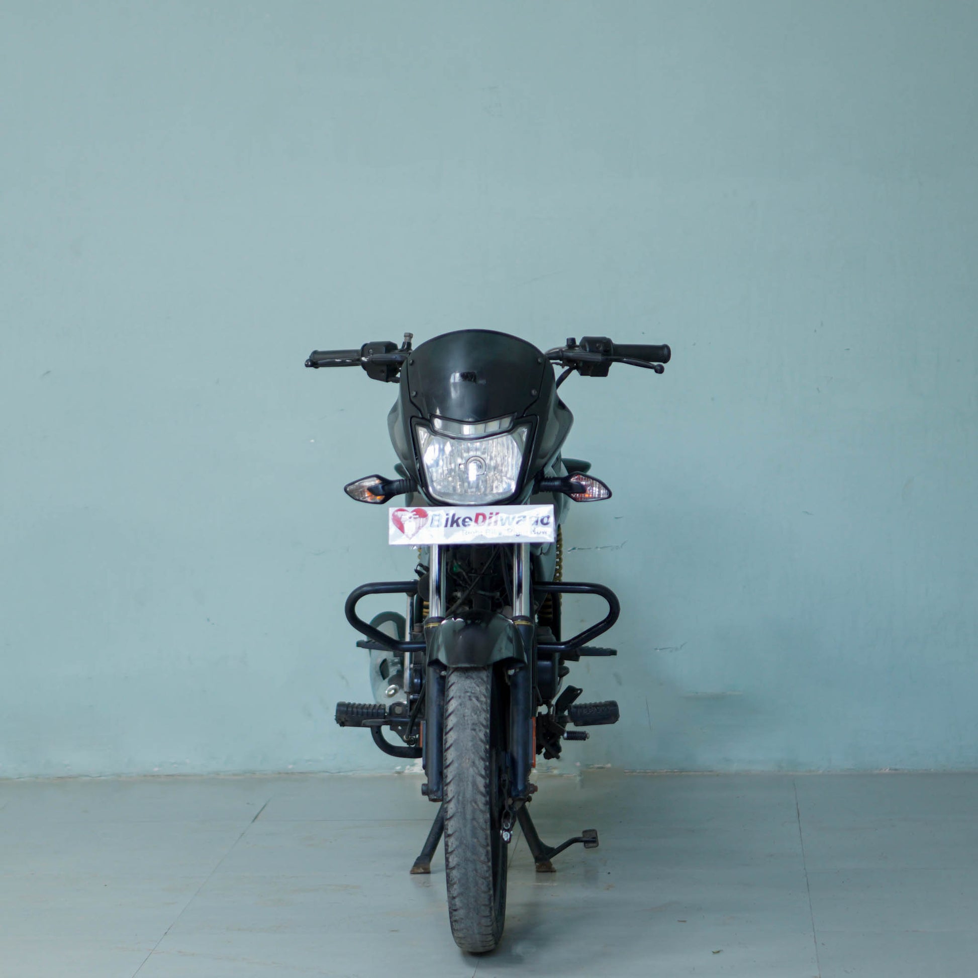 Bajaj Platina motorcycle from BikeDilwado with a sleek design and black finish, parked on a city street.