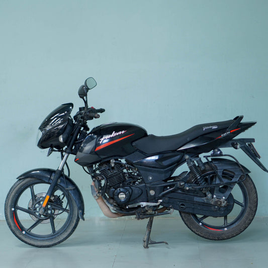 Bright red Bajaj Pulsar 125 motorcycle with sporty design and alloy wheels, parked on a city street.