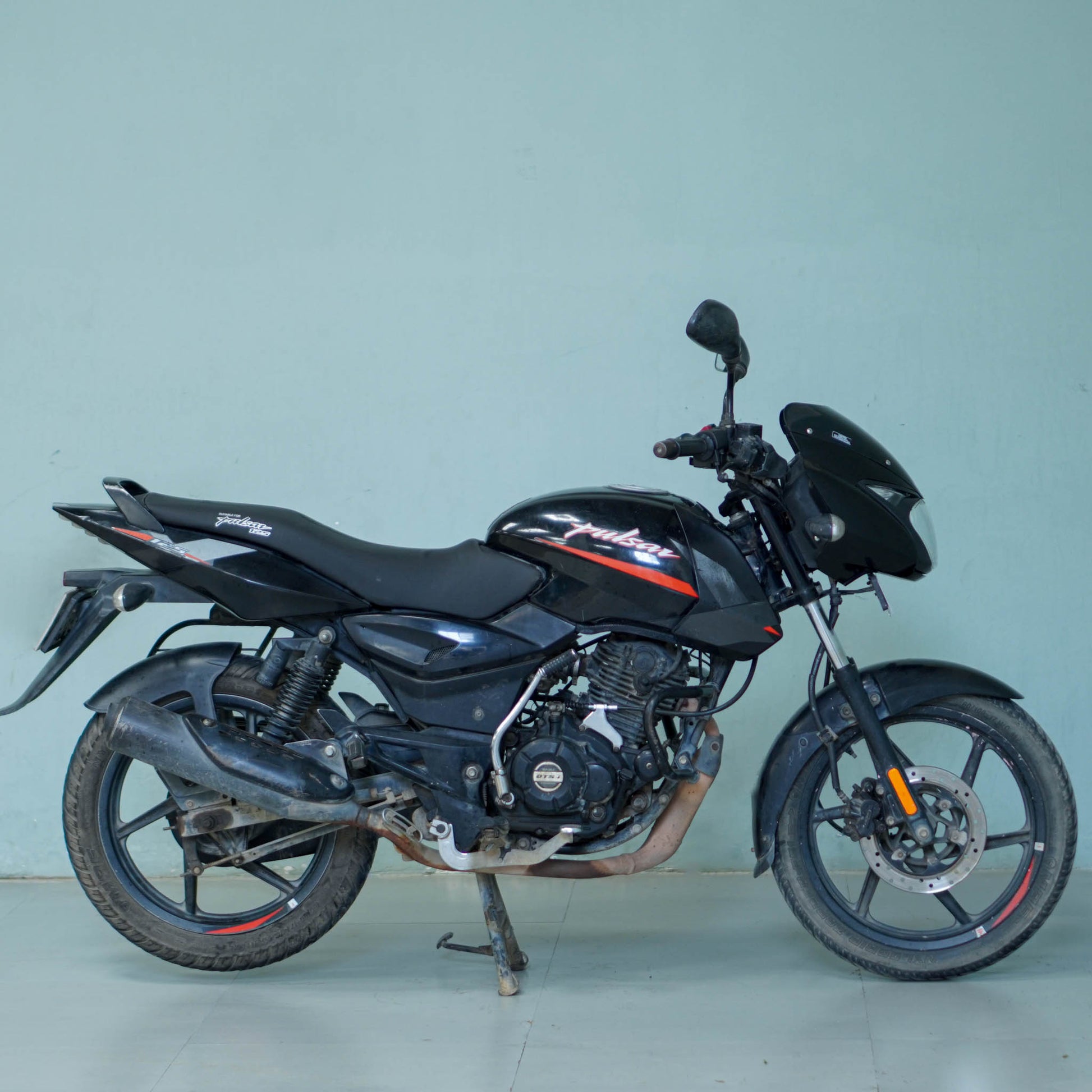 Black Bajaj Pulsar 125 motorcycle with sporty design and sleek body, parked on a city street.