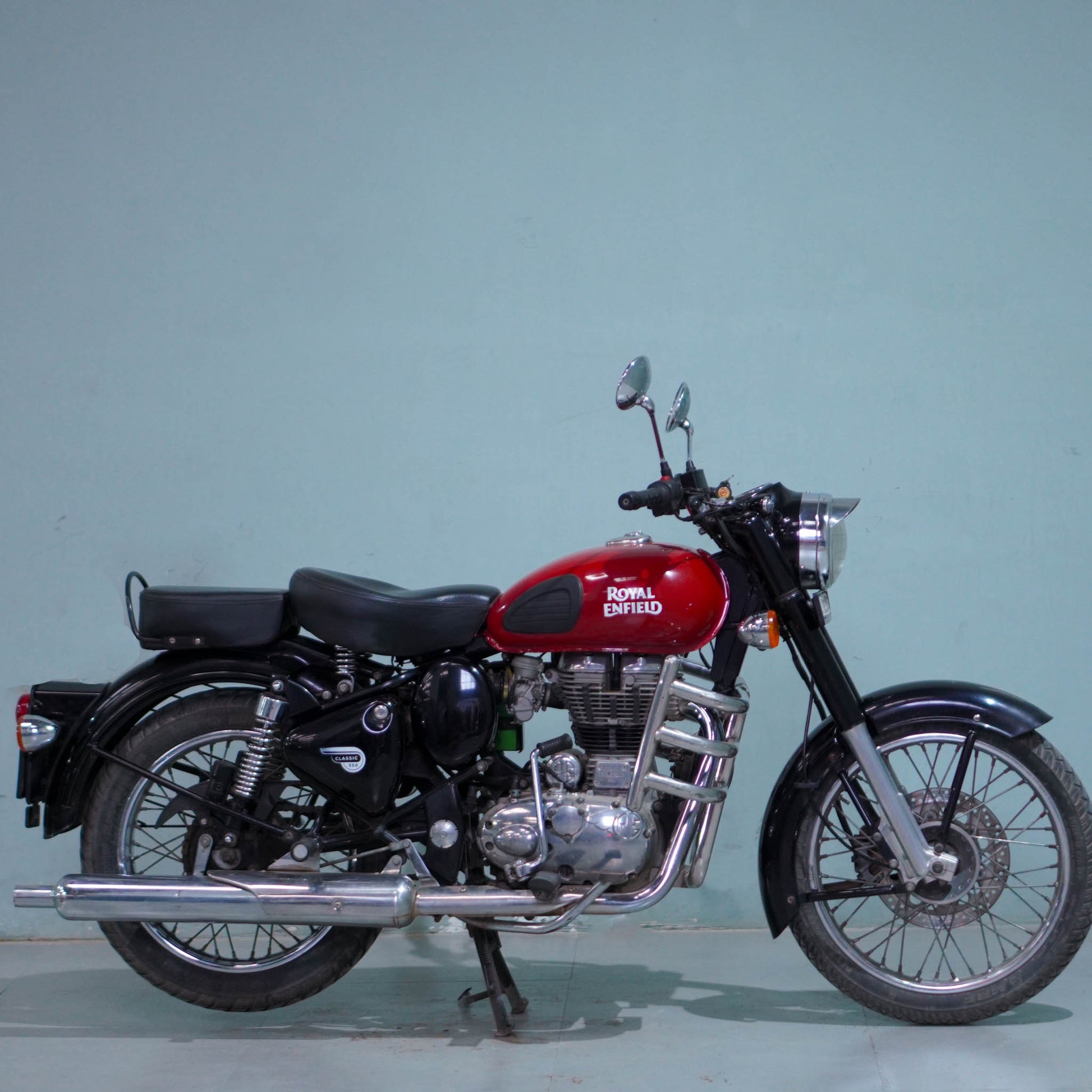 Royal Enfield Classic 350 motorcycle with black fuel tank, chrome accents, and vintage styling, parked on a scenic road.