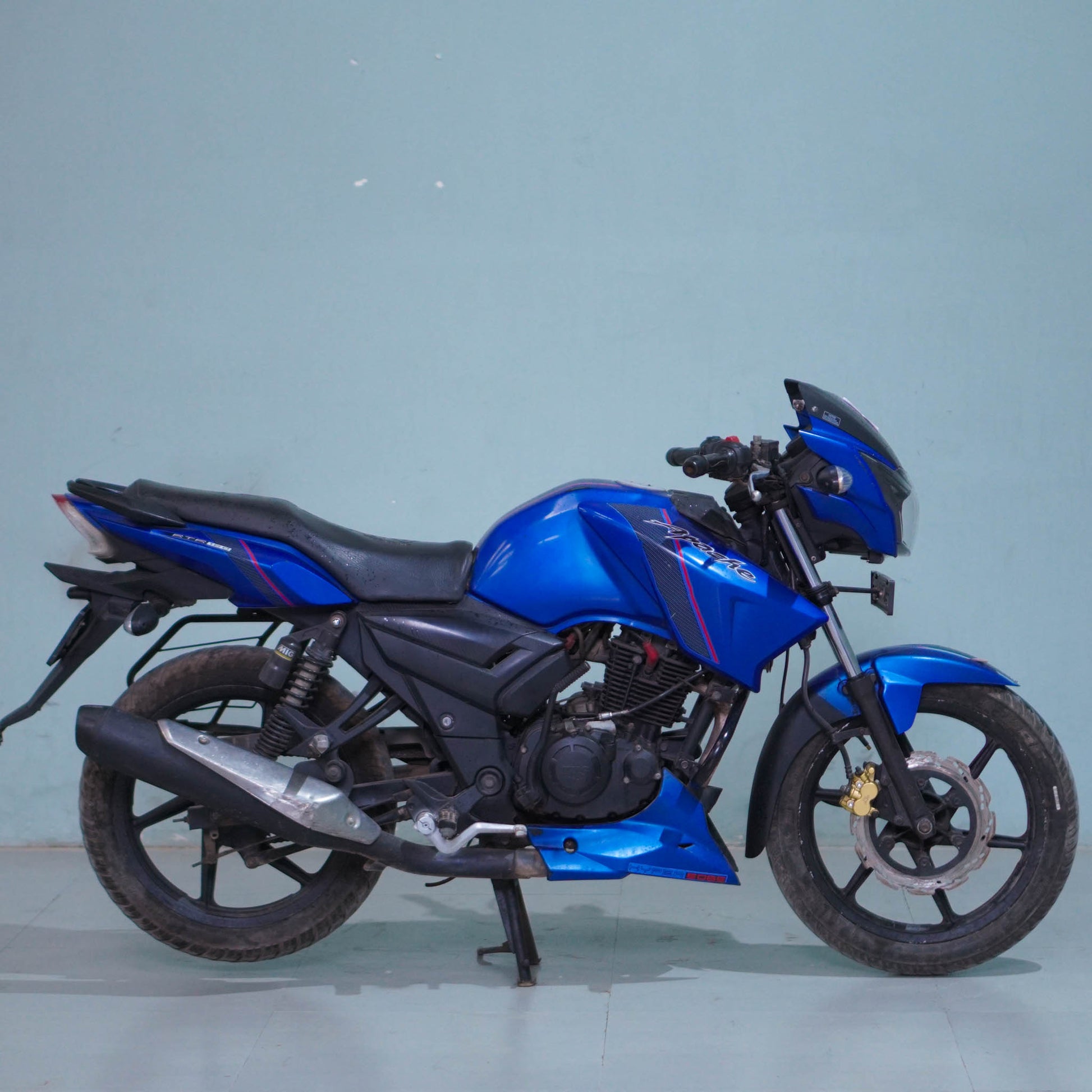 TVS Apache 160 motorcycle parked on a road, showing its sporty design and bold black and red color scheme.