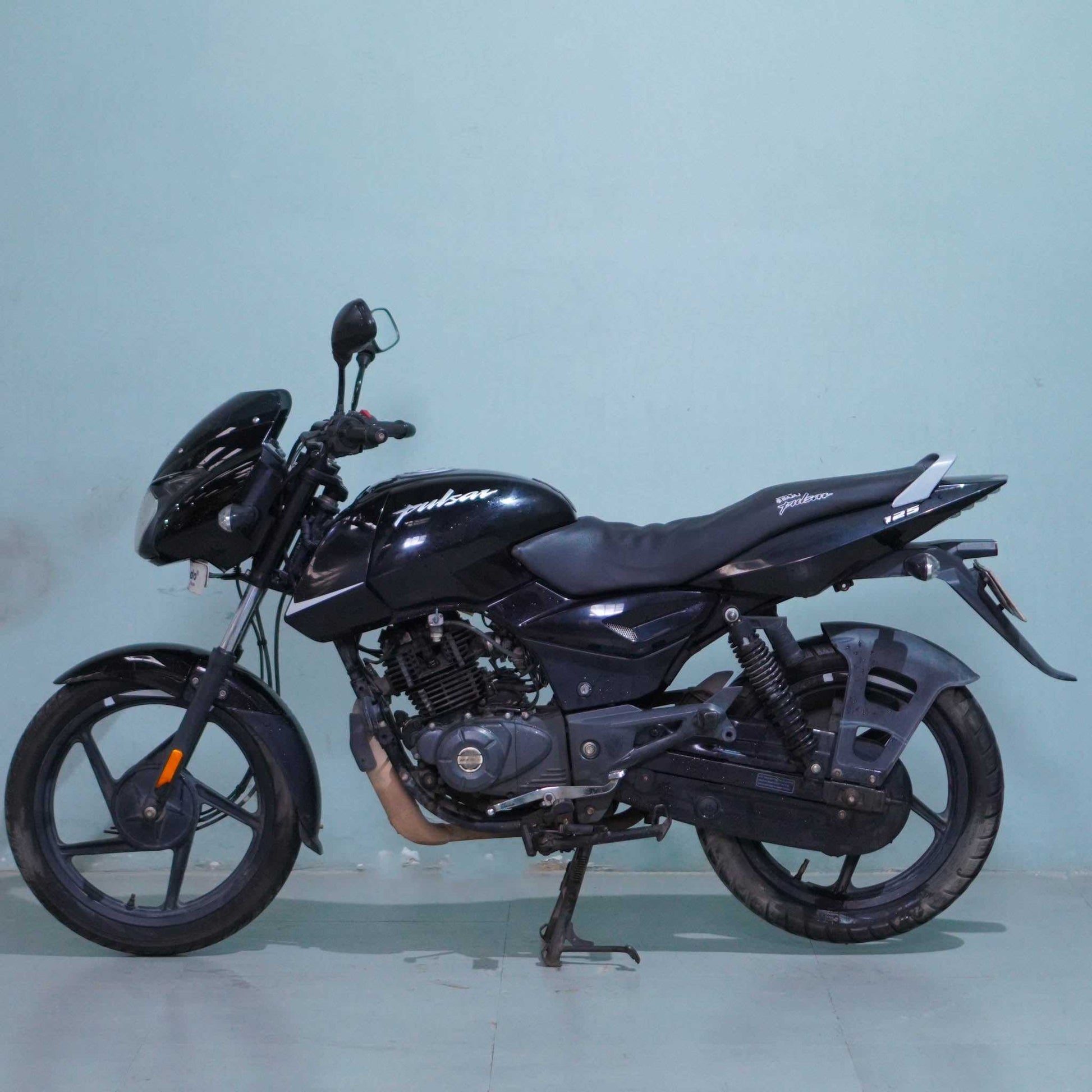 Black Bajaj Pulsar 125 motorcycle with sporty design and sleek body, displayed on a stand.