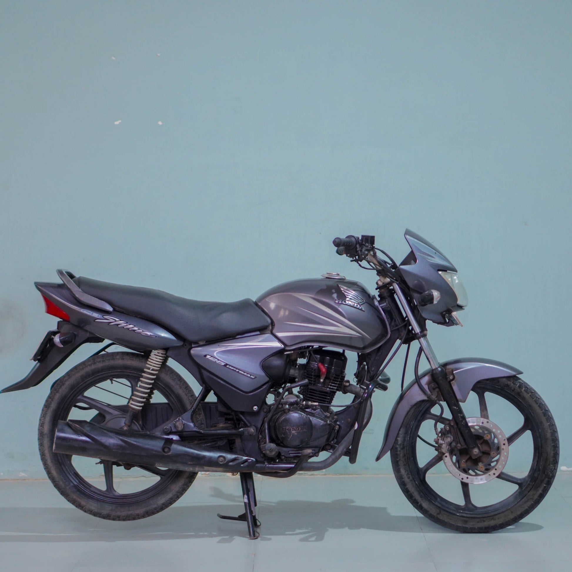 Honda Shine 125 motorcycle from BikeDilwado with a shiny silver body and black accents, parked on a street.